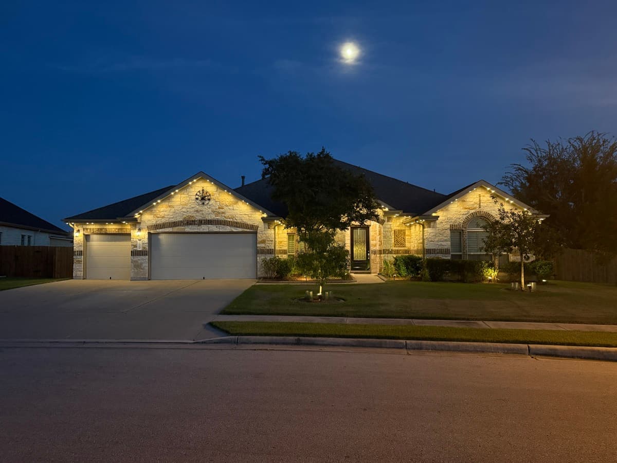 Austin Hill Country single-story limestone ranch home at dusk illuminated with TruLight permanent lighting in warm white