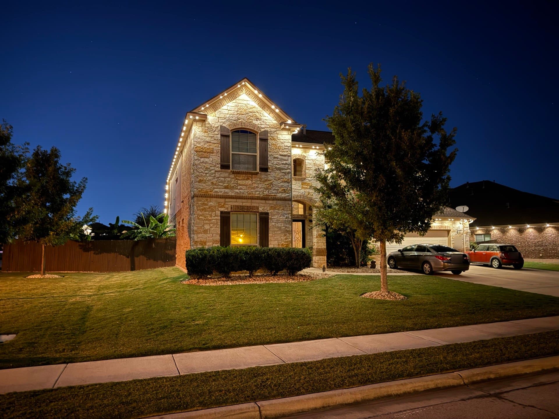 Two-story limestone home in the Austin area with warm white permanent roofline lighting at dusk