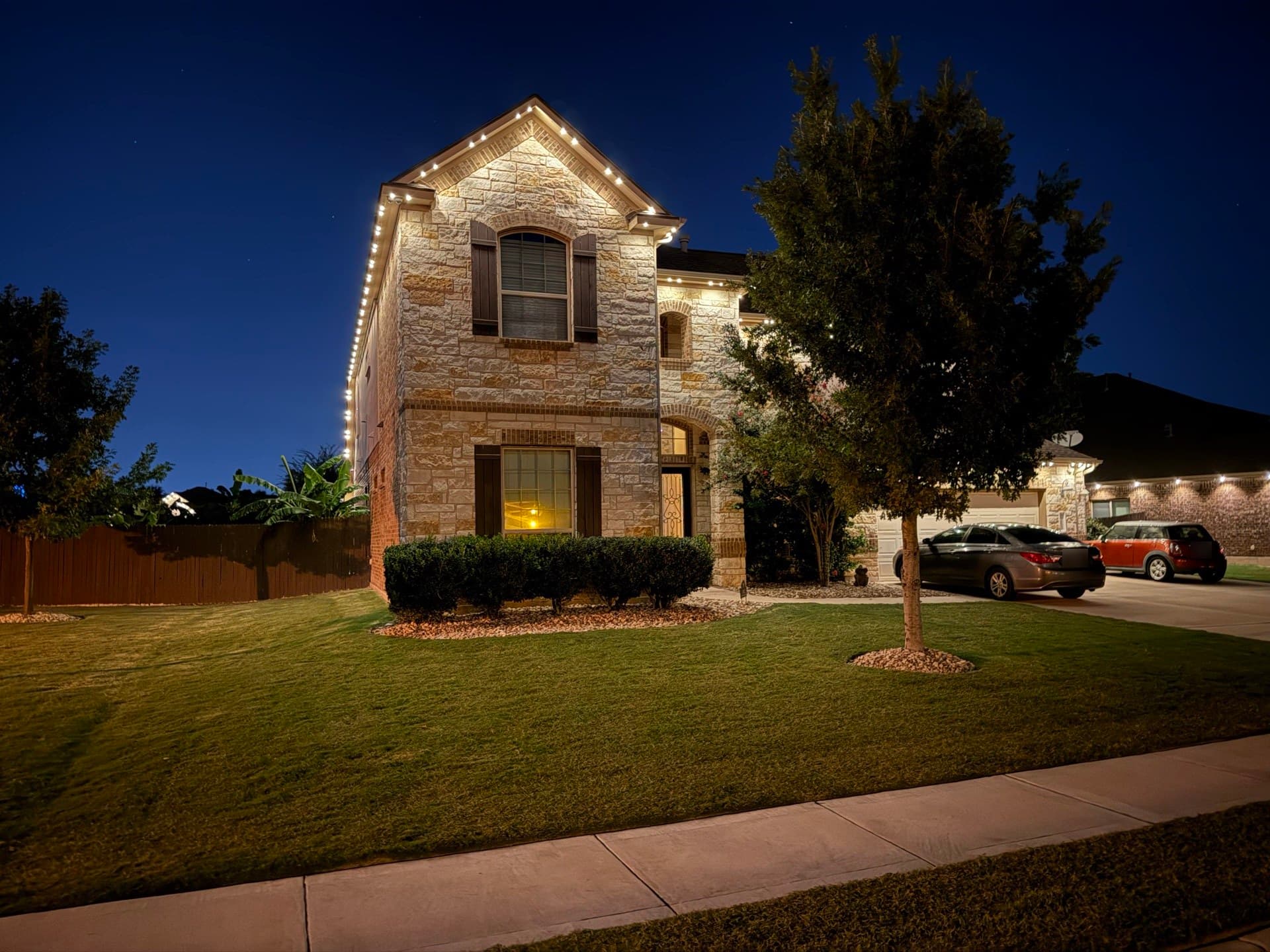 Evening view of a two-story limestone Austin-area home with warm white permanent roofline lighting