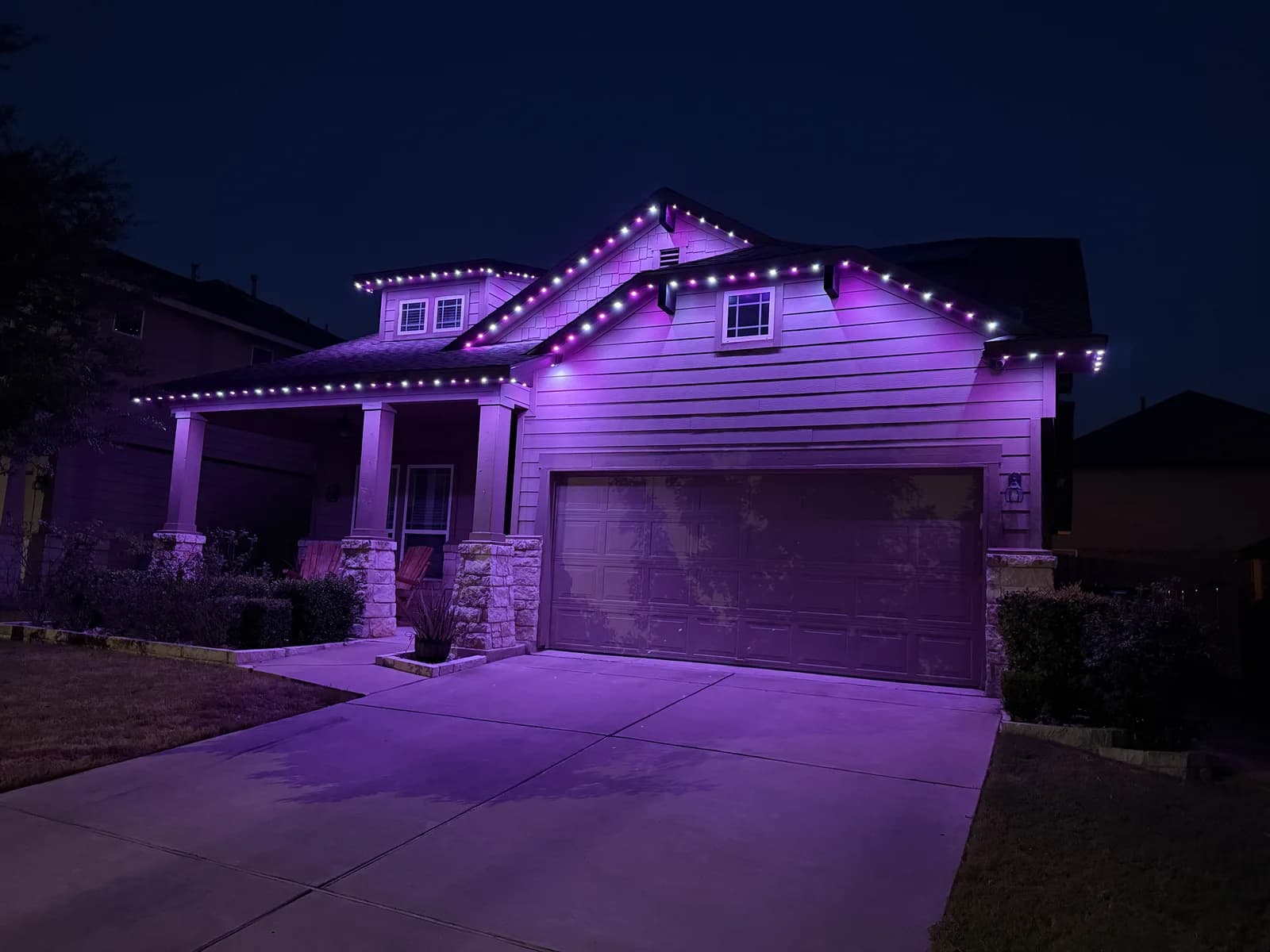 Purple and white roofline lights on a Pflugerville home with stone porch columns.