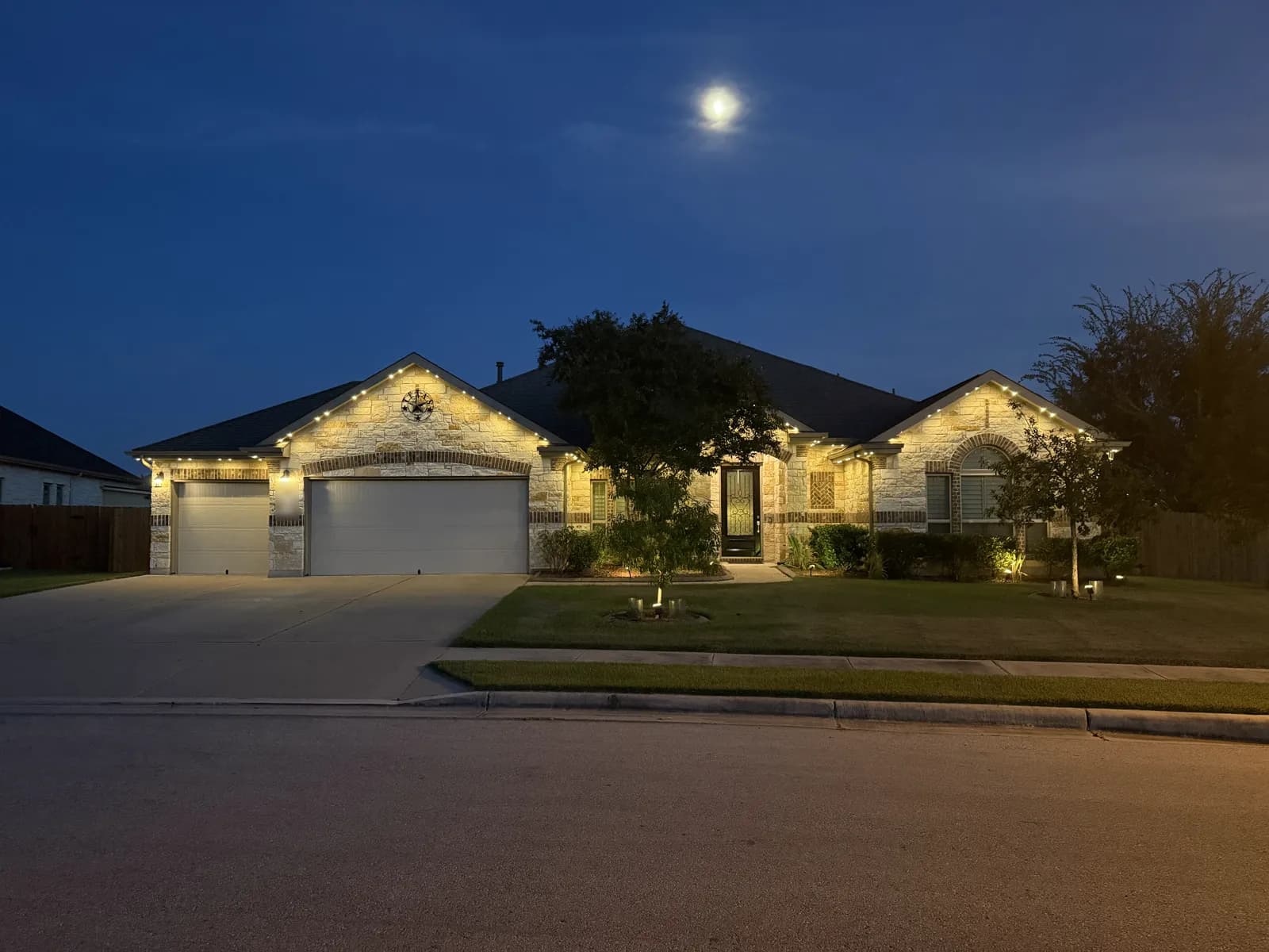 Warm white roofline lights on a single-story Pflugerville home with a stone front and two garage doors.