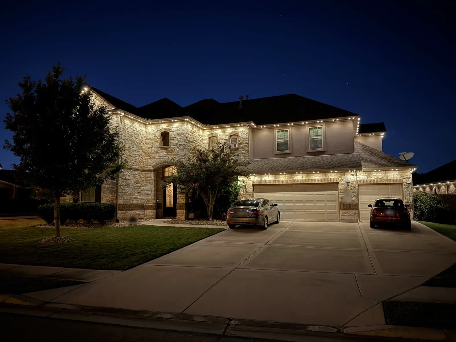 Warm white lights along the roofline of a two-story stone home in Pflugerville.
