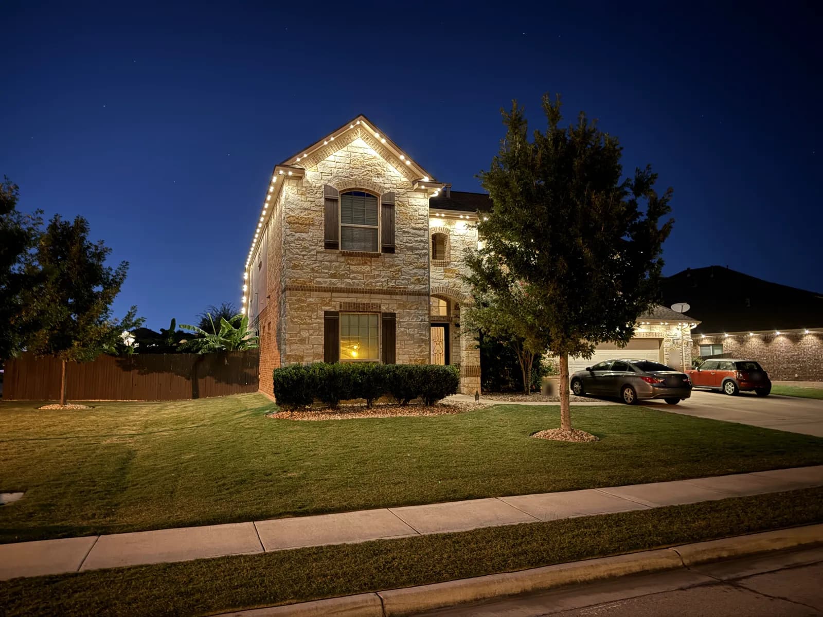 Warm white lights outline the front gable of the same two-story Pflugerville home.