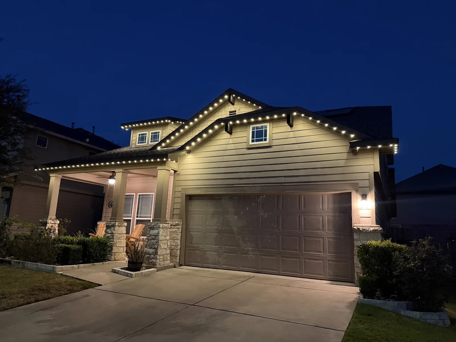 Warm white roofline lighting on a Pflugerville home with a covered porch and front garage.
