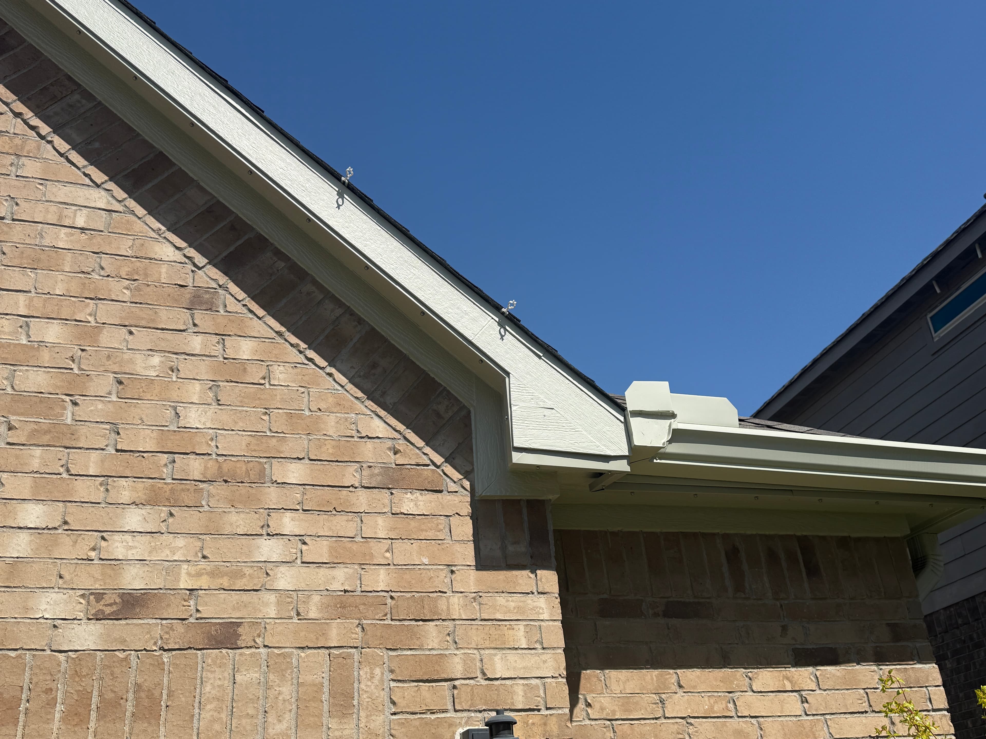Daylight close-up of a Trimlight installation along a pale fascia above a brick exterior