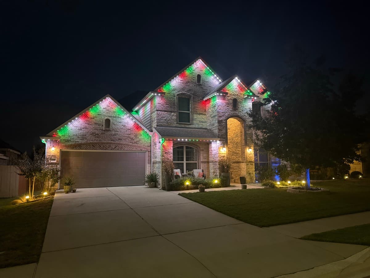 Warm white permanent LED lighting on a two-story Austin Hill Country stone home at dusk